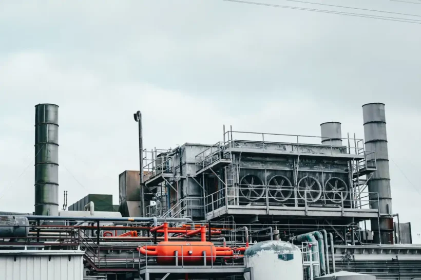 Instalação industrial com sistema de dutos e tubulações, estruturas metálicas e chaminés ao fundo, mostrando um ambiente de produção que requer manutenção industrial para otimizar a operação.
