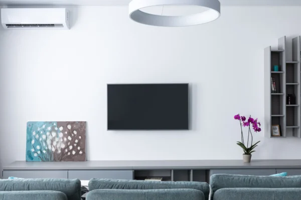Sala moderna com sofá cinza, televisão na parede, iluminação de teto e ar-condicionado split instalado na parede, ilustrando conforto e eficiência em climatização